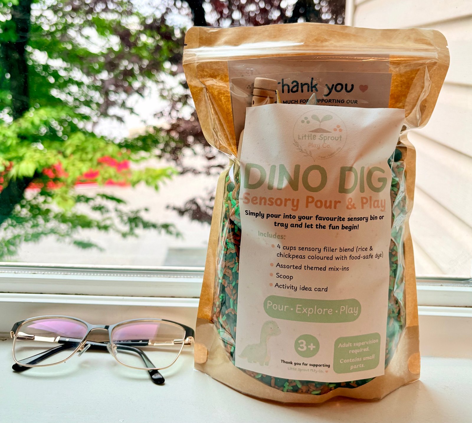 Dino Dig ready-to-pour dinosaur sensory play kit in a resealable bag sitting beside a pair of glasses to show size comparison.