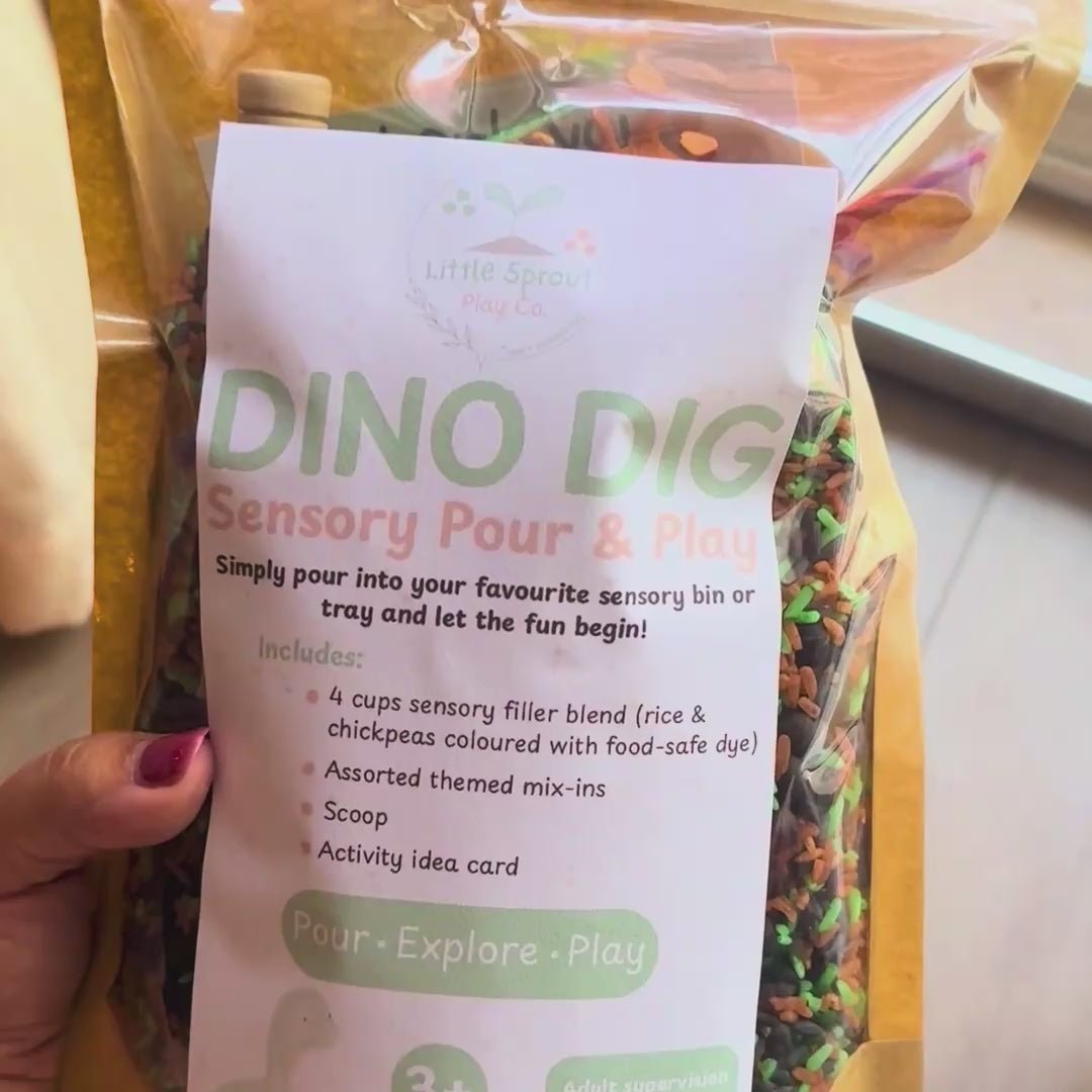 contents of dino dig sensory play kit poured out to show colourful green, brown, black rice, with green pasta resembling bushes or trees, and 5 dinosaur play pieces, and a wooden scoop.
